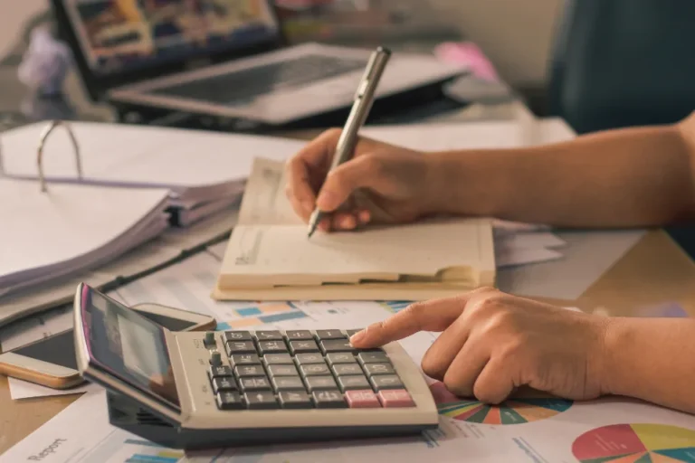 Entrepreneur reviewing business income and personal pay calculations at a desk with a calculator